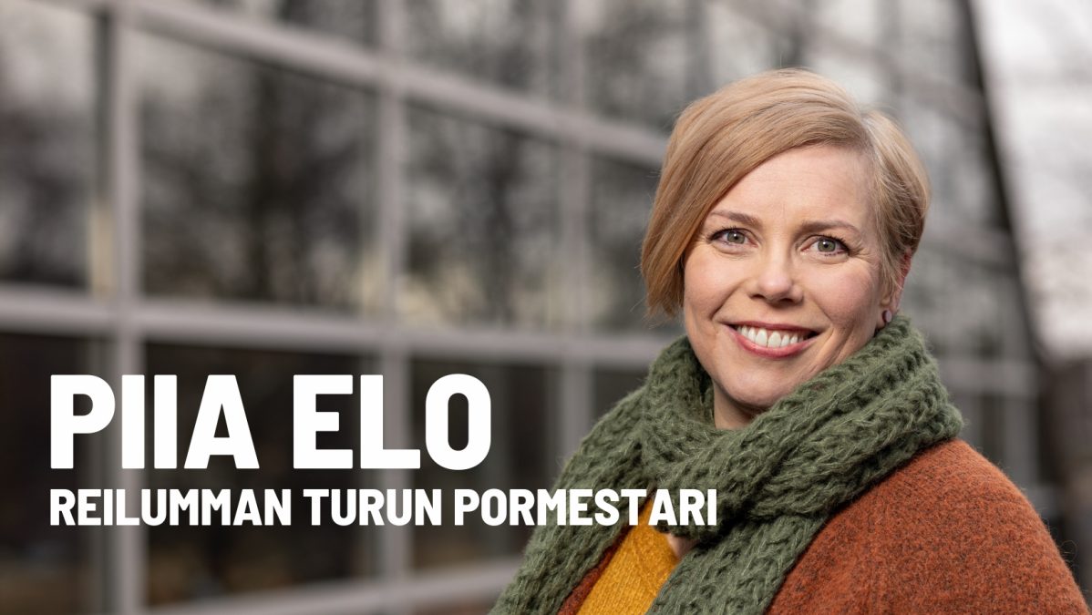 Piia Elo hymyilemässä kameralle vihreä kaulahuivi kaulalla. Kuvassa teksti Piia Elo reilumman kaupungin pormestari.